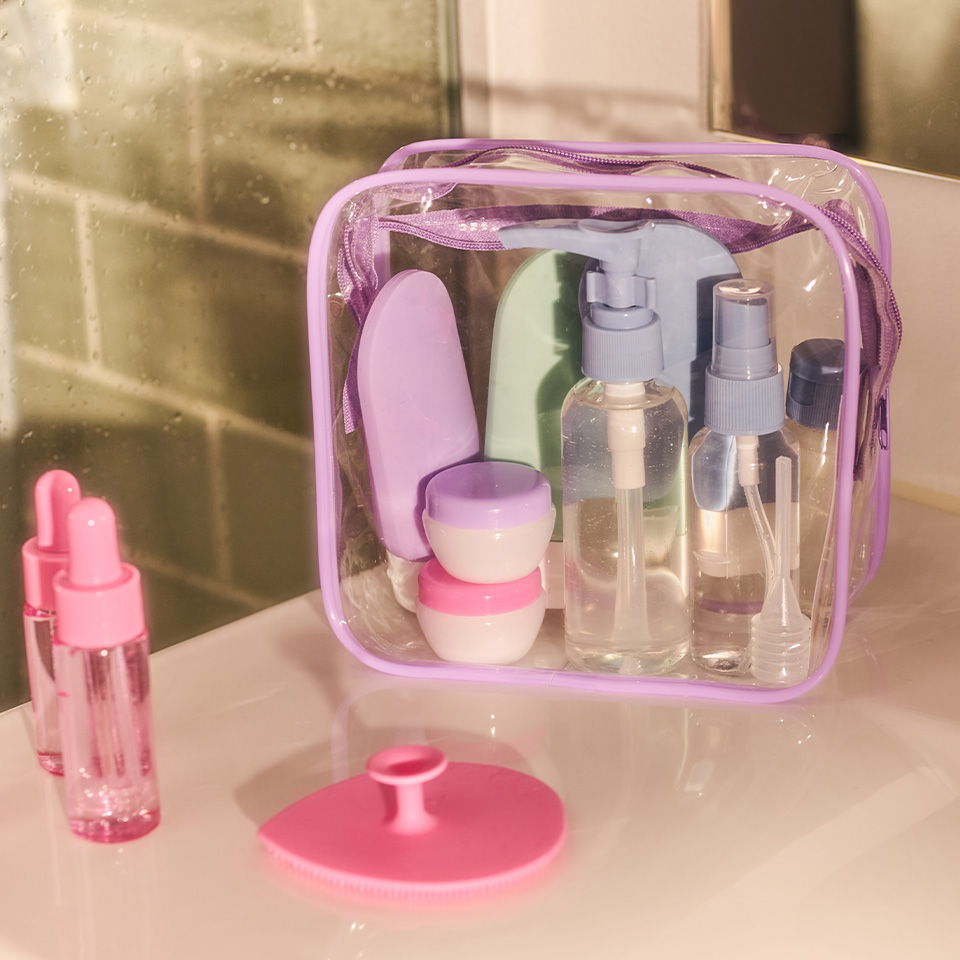 Clear cosmetic bag with various bottles and containers in pastel colors.