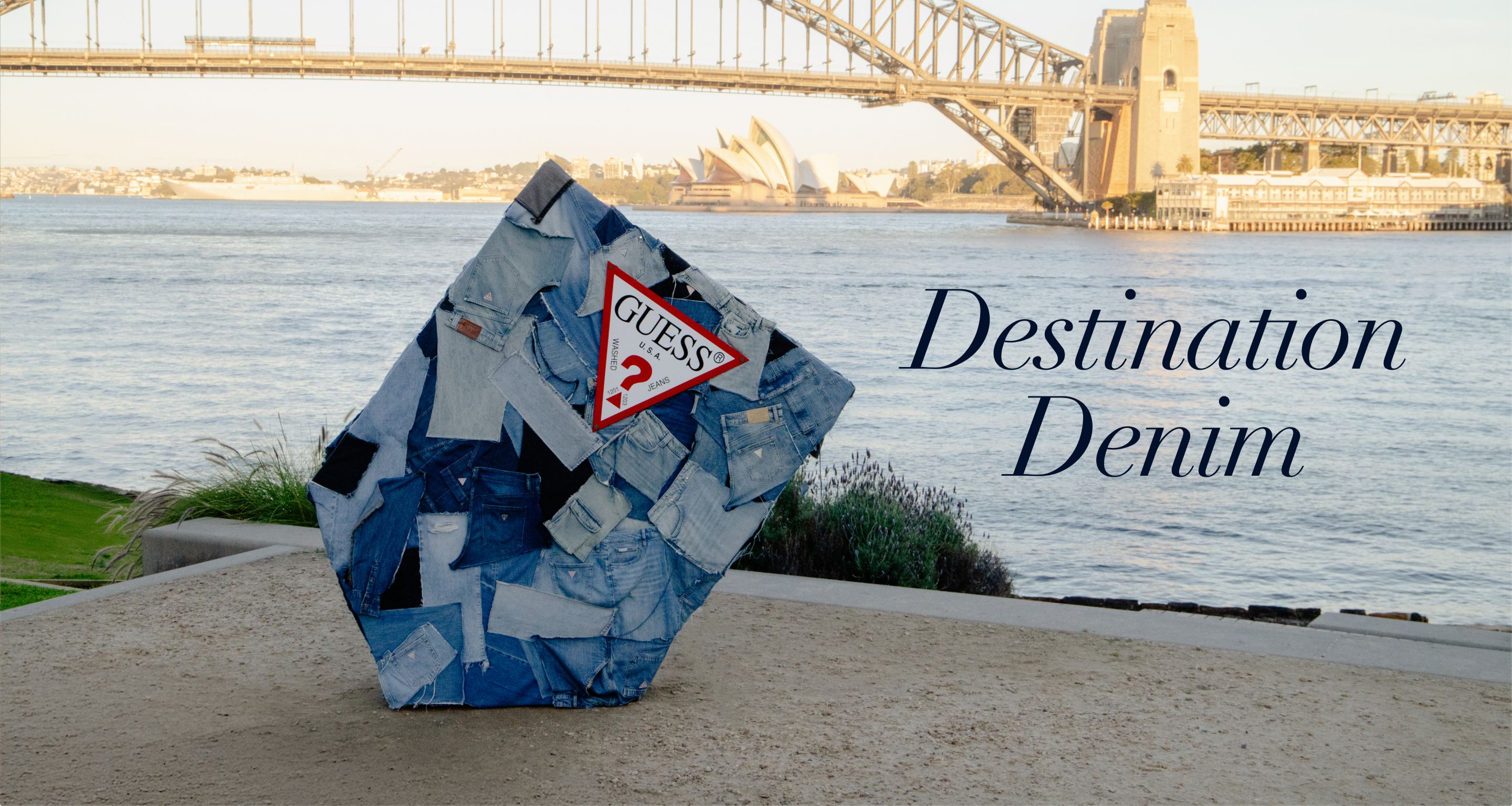 A blue GUESS denim sculpture near a body of water with the Harbour Bridge in the background.