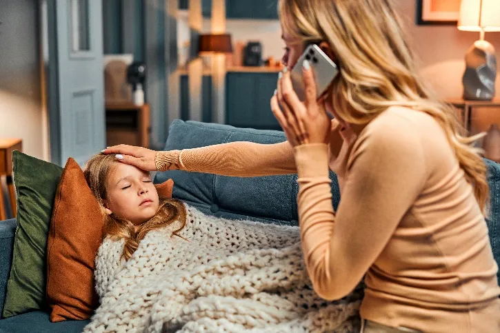 Eine besorgte Mutter ruft den Rettungsdienst für ihre Tochter, die auf dem Sofa liegt, da sie vermutet, dass ihre Tochter eine Anaphylaxie hat.