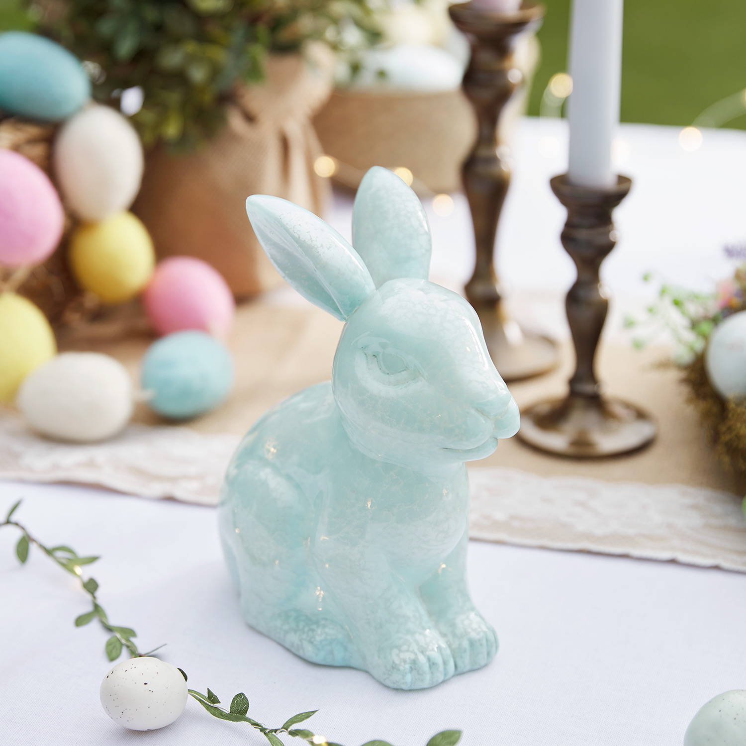 Blue glass bunny light on an Easter table display with garlands and candles.