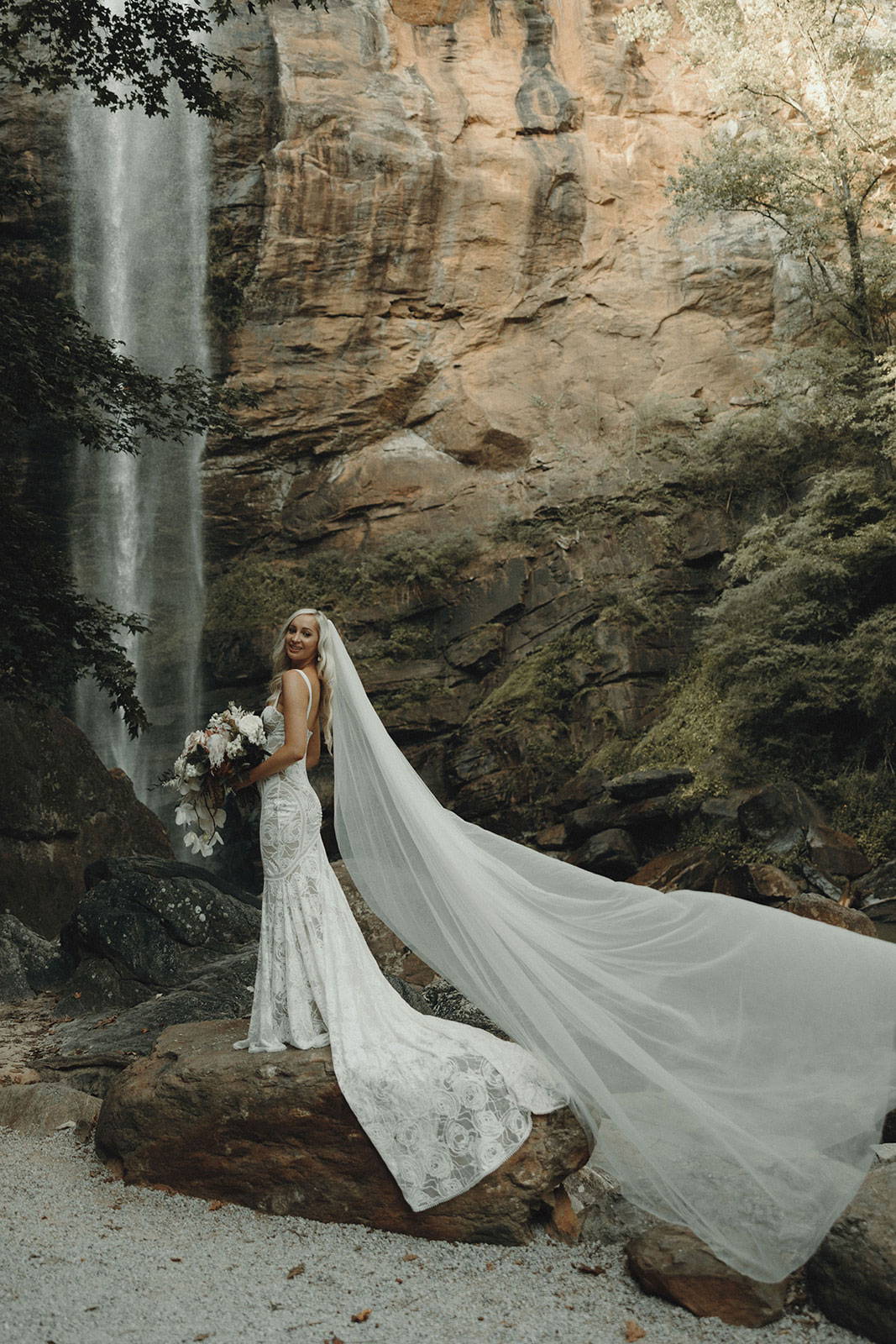 Bride standing on rock in front of waterfall