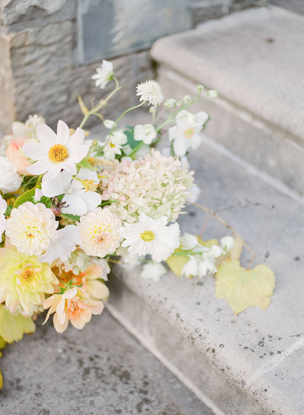 close up of white, peach and yellow bridal bouquet resting on stairs