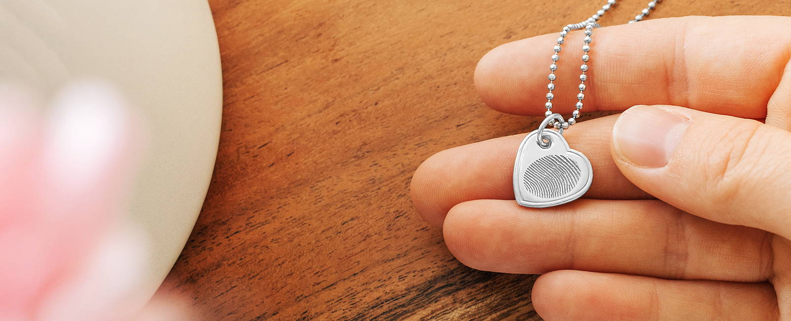 person holding a sterling silver heart charm fingerprint necklace