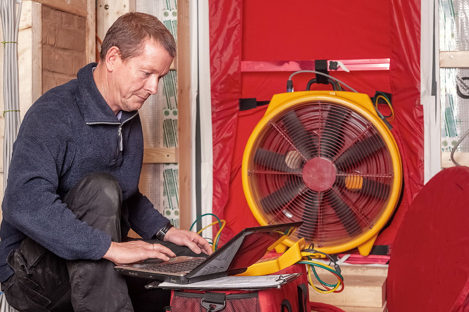 A technician using a laptop near a large ventilation fan.