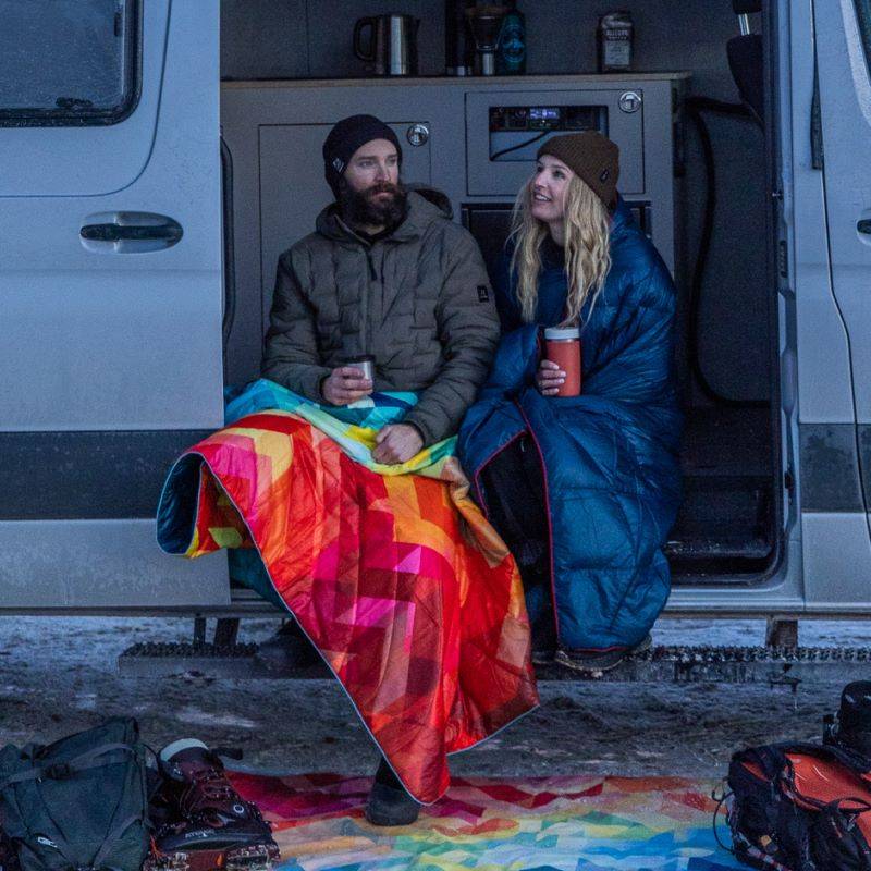 Two people sitting outside of a camper van in the snow.