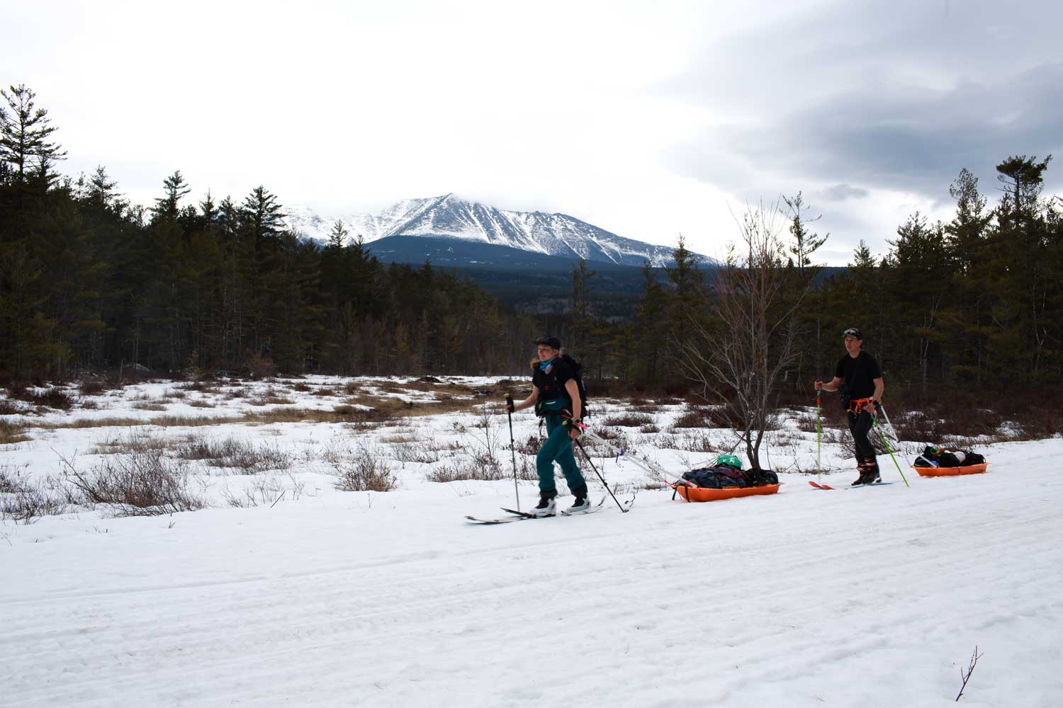Two people splitboarders in snowy landscape with mountains in background.