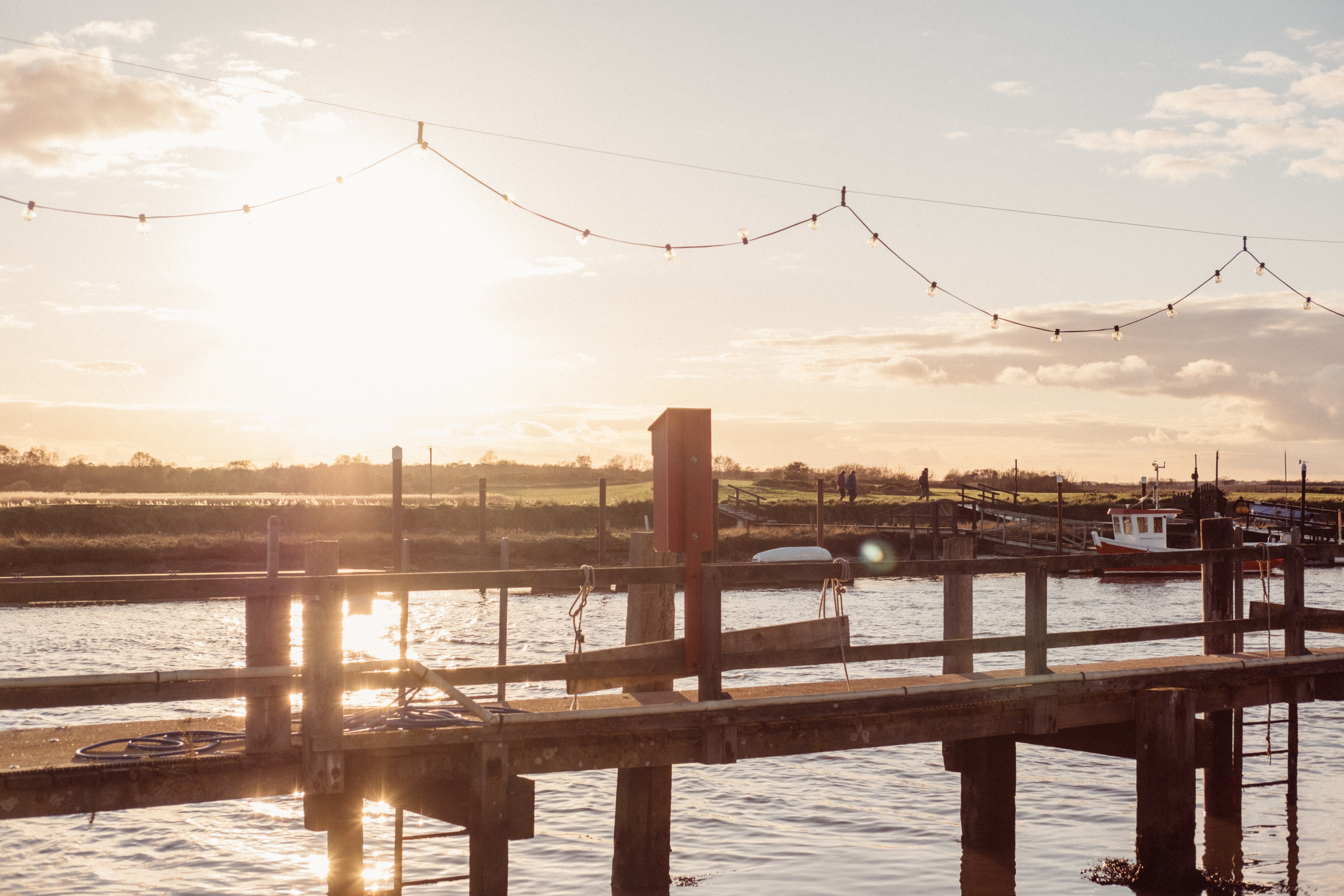 Sunset over a wooden pier with boats and decorative lights.
