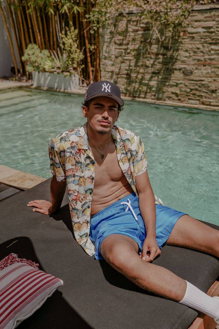 male model wearing maison article button up and shorts sitting on pool chair