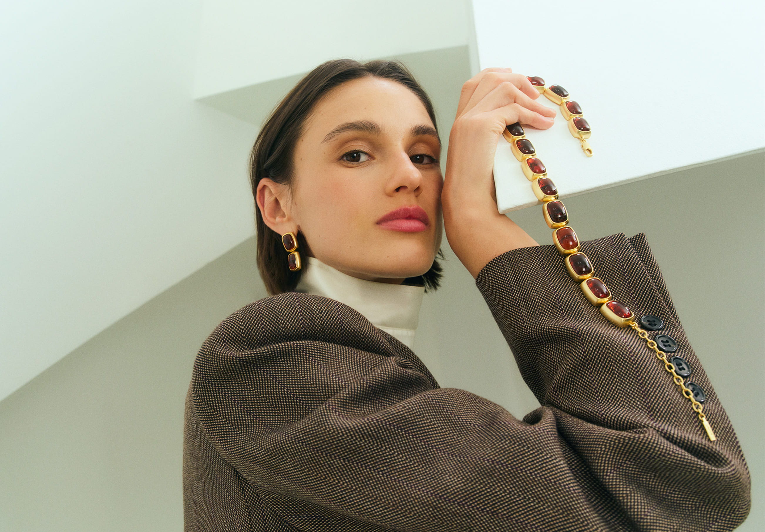 A woman poses with a stylish outfit and accessories against a minimalist background.