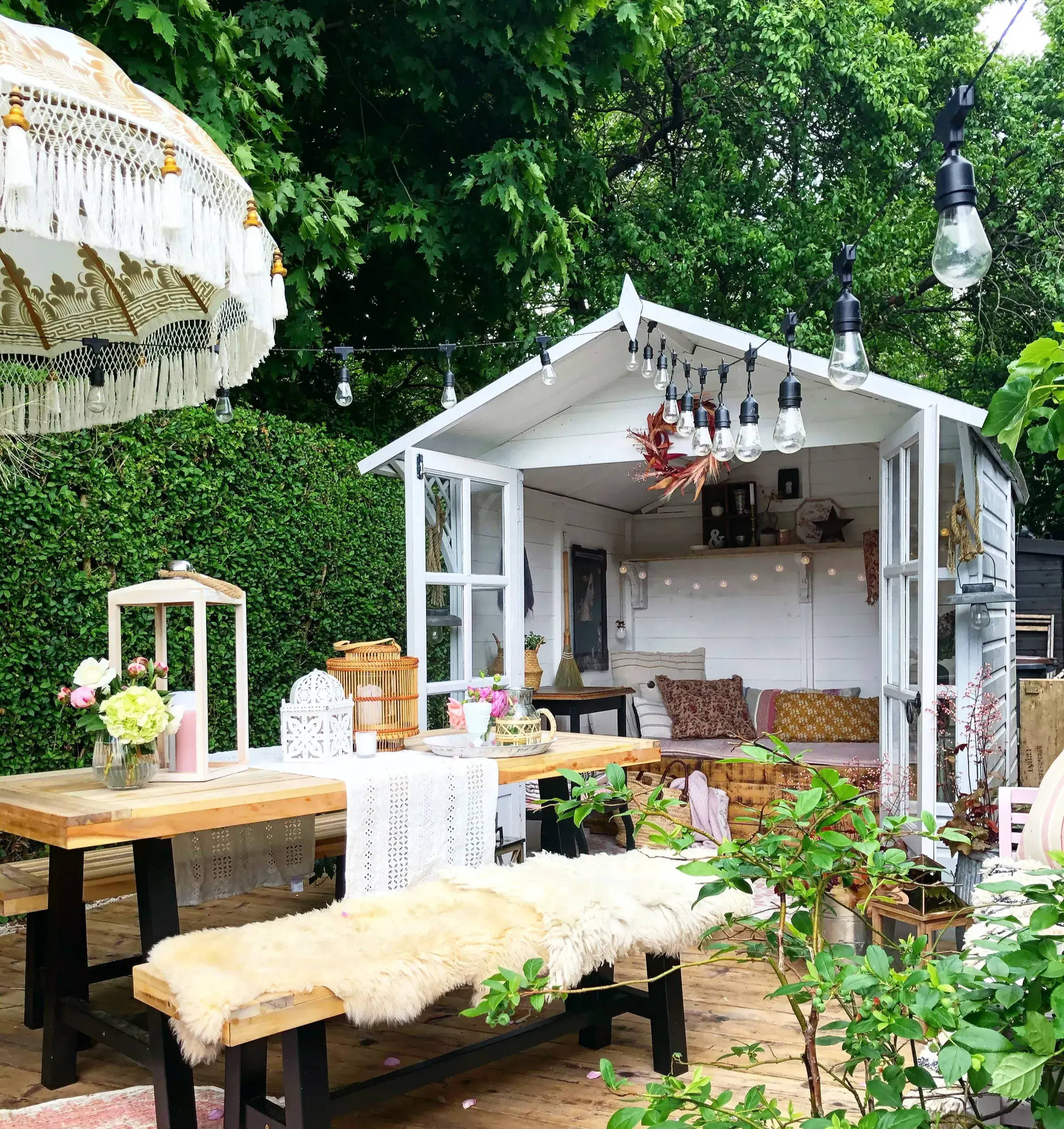 Festoon lights hanging over a summer bench and seating area with a garden shed in the background.