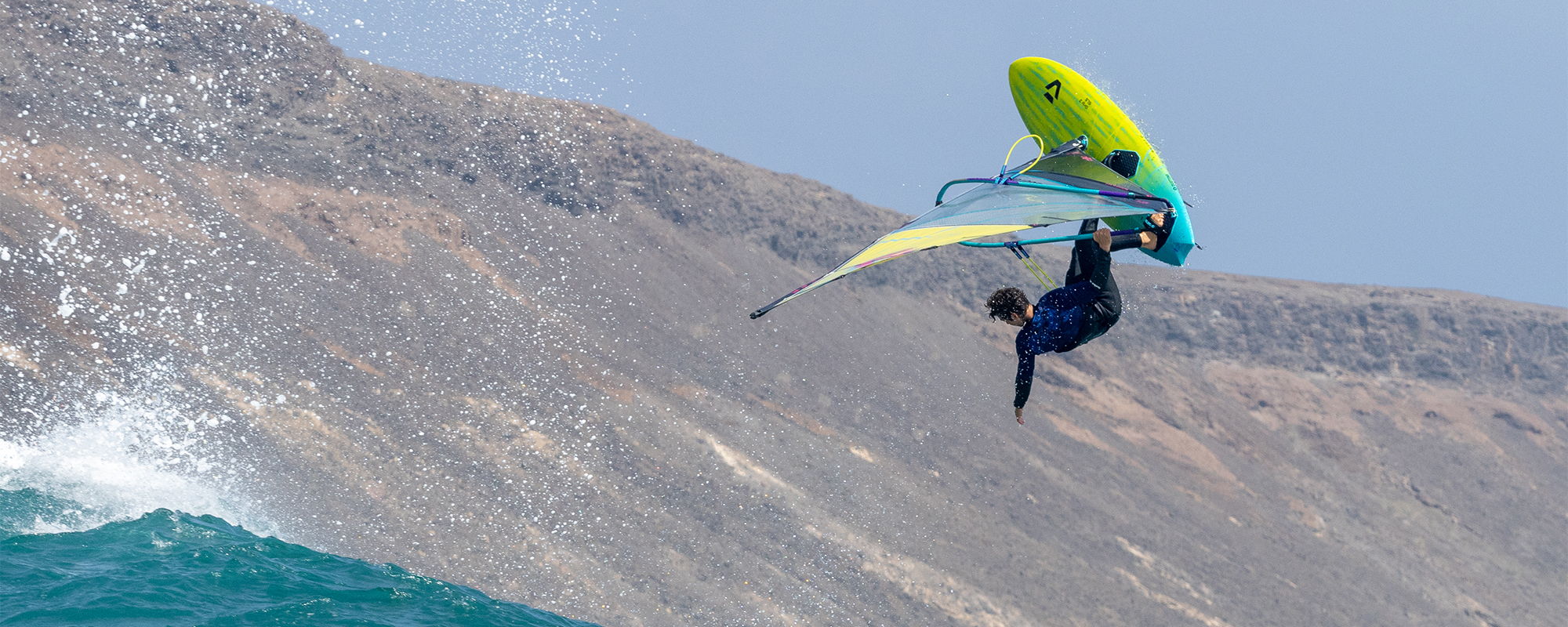 Une personne faisant du windsurf au-dessus de l'eau, avec les montagnes en arrière-plan.