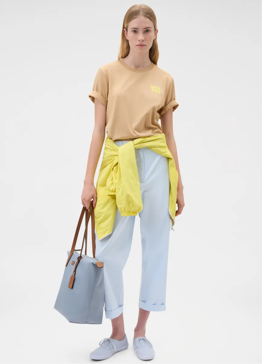 Young woman in casual attire holding a bag, with a yellow jacket around her waist.