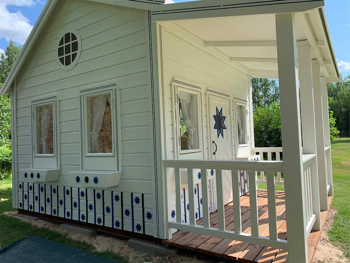 White custom playhouse with glass windows and a porch by WholeWoodPlayhouses