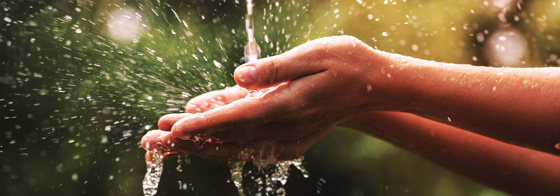Hands cupping water, droplets splashing in a natural setting.