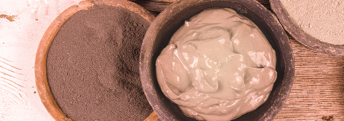 Bowls containing different types of clay or mud on a wooden surface.
