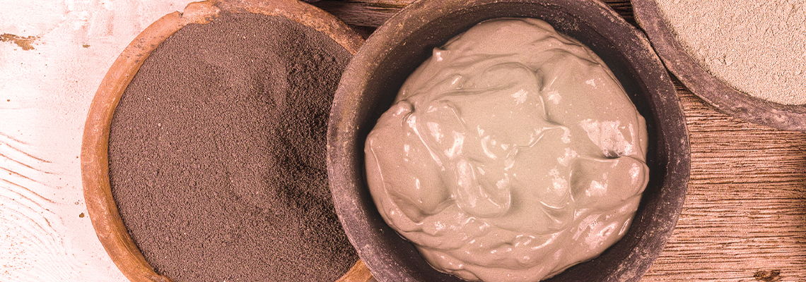 Bowls containing different types of clay or mud on a wooden surface.
