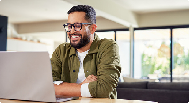 Smiling man working on a laptop in a bright, modern room.