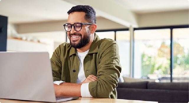 Smiling man working on a laptop in a bright, modern room.