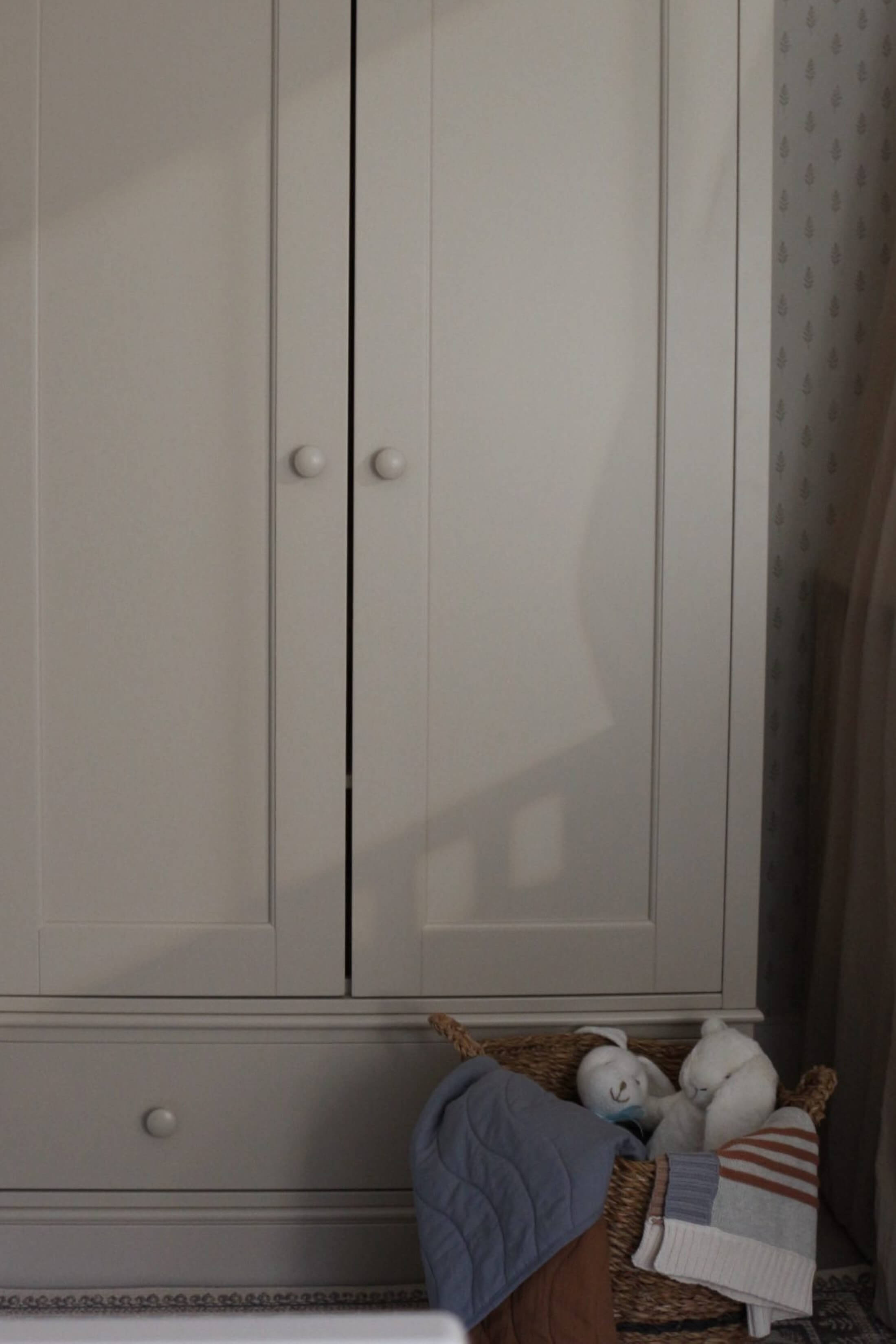 A light-colored wardrobe with a basket of textiles nearby.