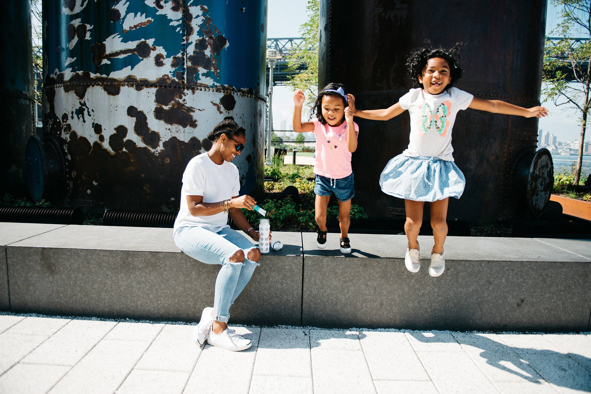 Children jumping off a ledge while their mother mixes Liquid IV's electrolyte powder into a water bottle.