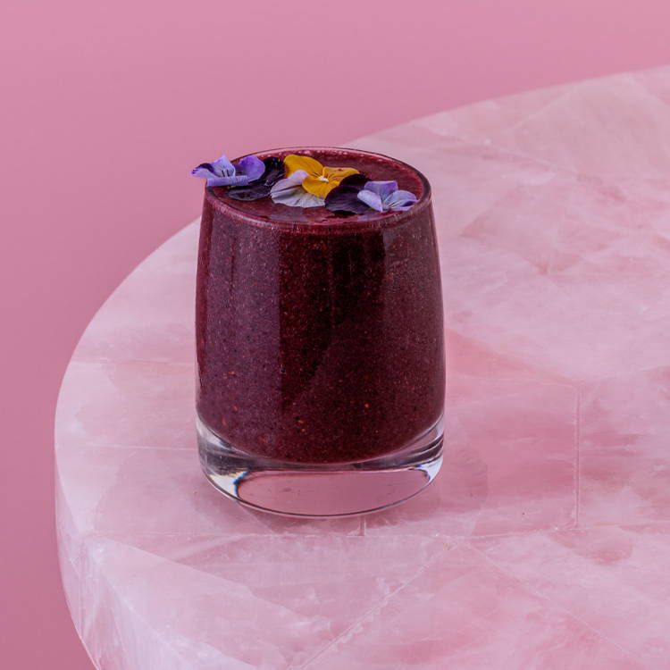 Blackcurrant and raspberry smoothie on pink backgroud with edible flowers