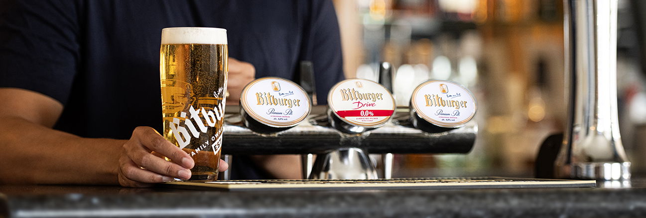 Bartender holding a fresh pint of Bitburger beer at a pub.