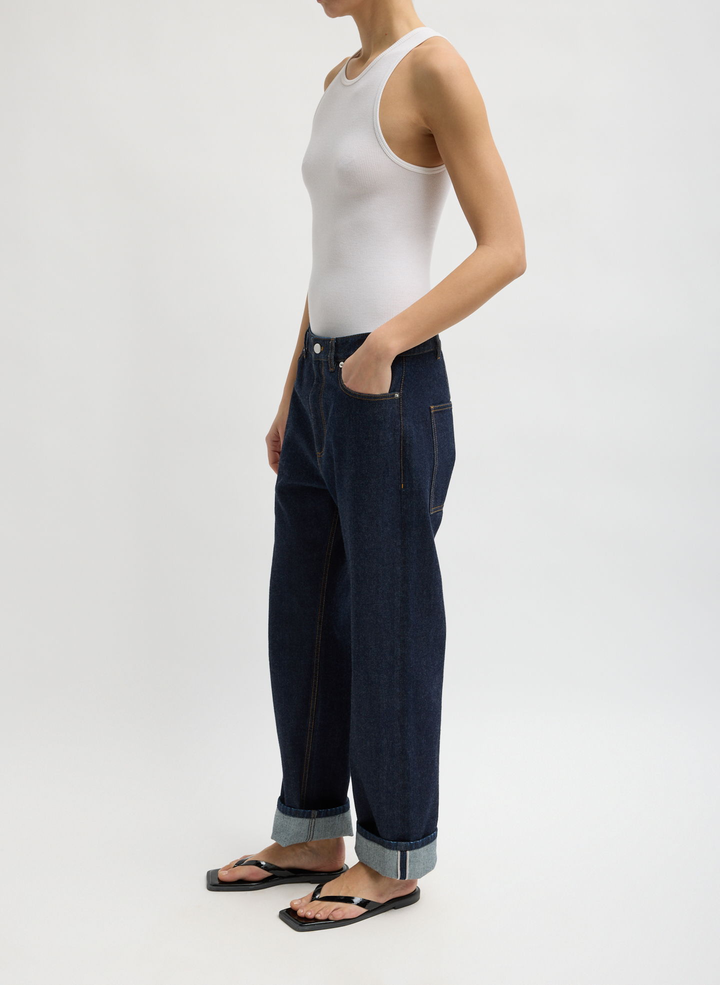 Person wearing a white tank top and loose blue jeans, standing sideways.