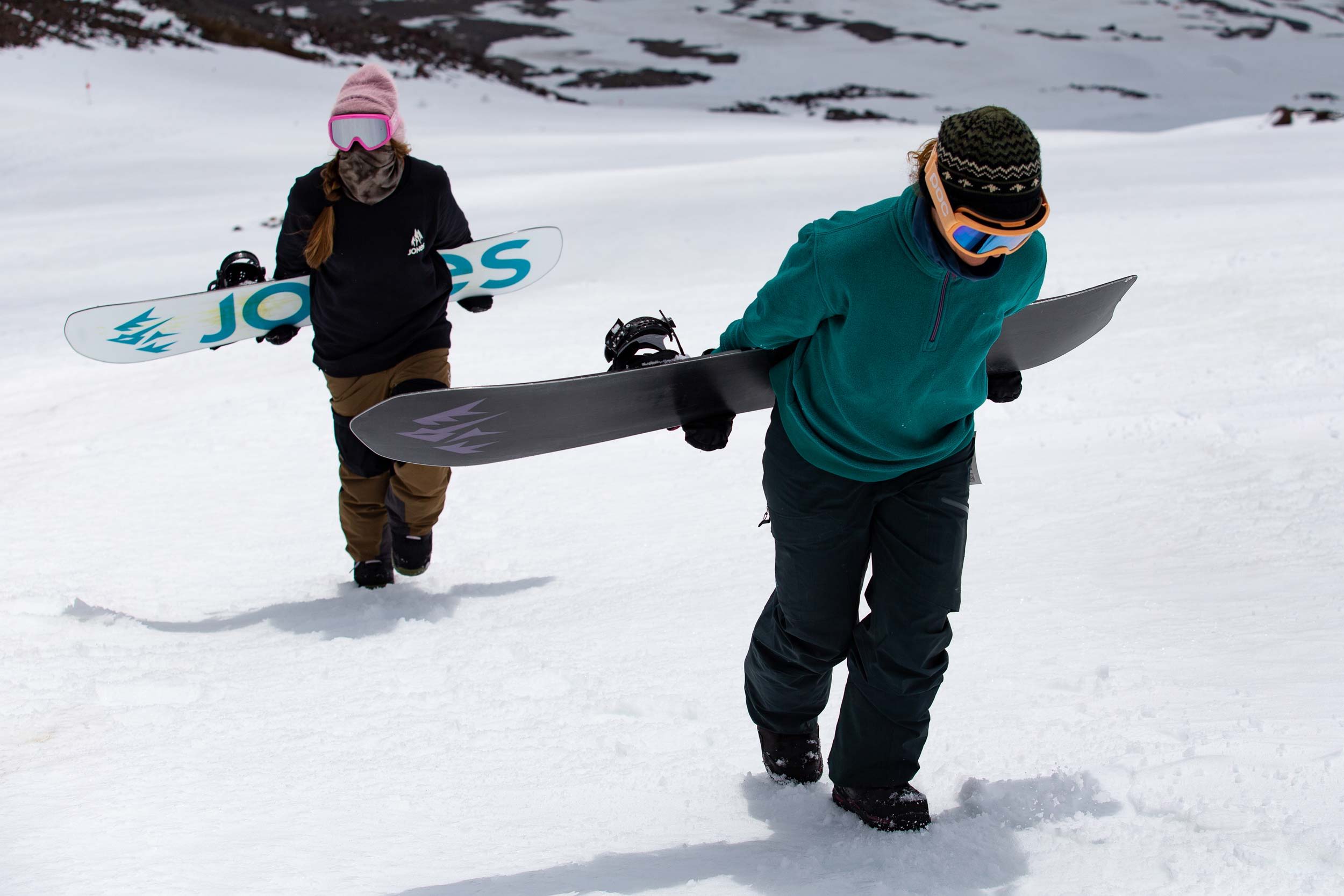 Two snowboarders walking on snow carrying their boards.