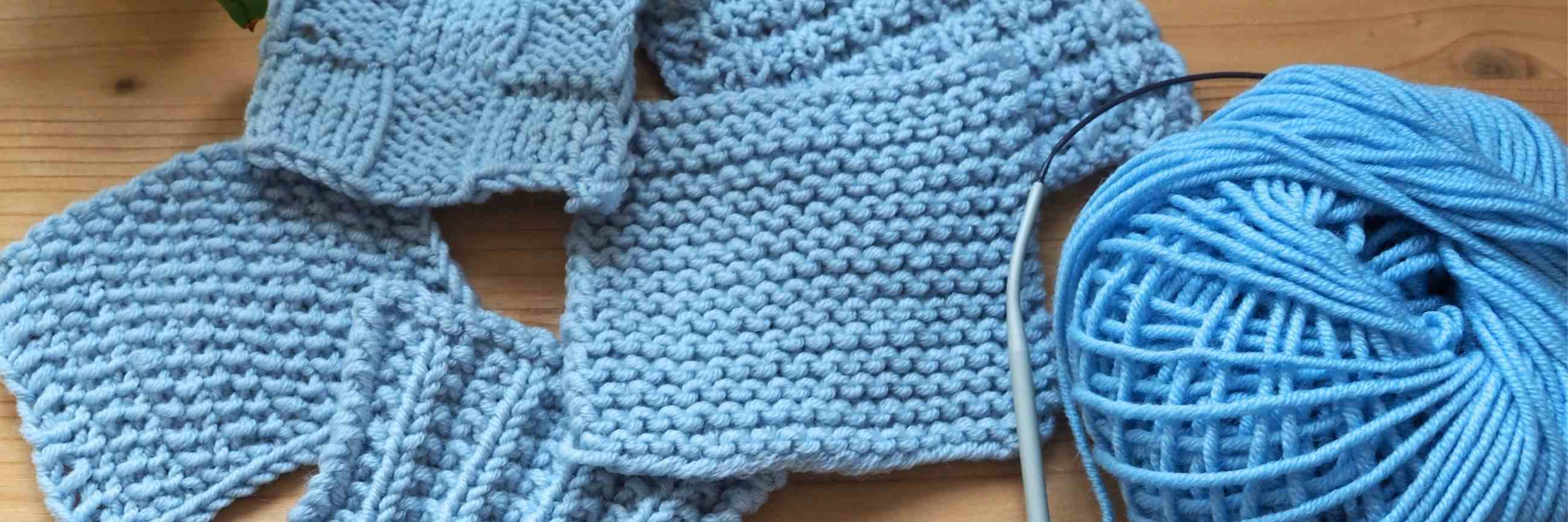 Nahaufnahmen von Maschenproben in unterschiedlichen Mustern aus hellblauem Garn auf einem Holztisch.