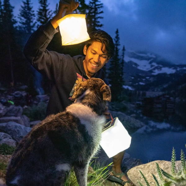 Man holds lanterns near his dog in mountains.