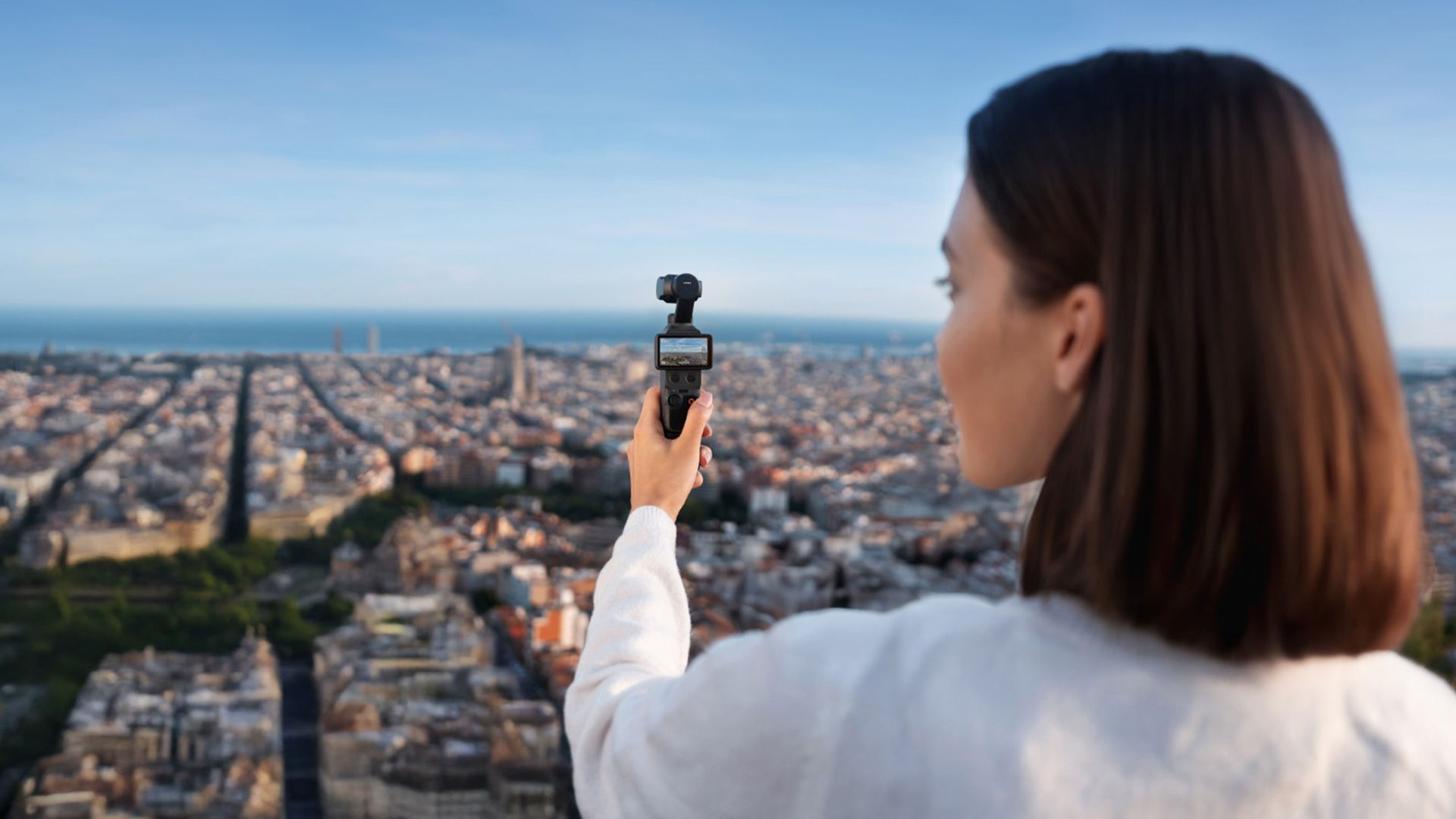 Woman holding a DJI Osmo Pocket 4 overlooking a cityscape.