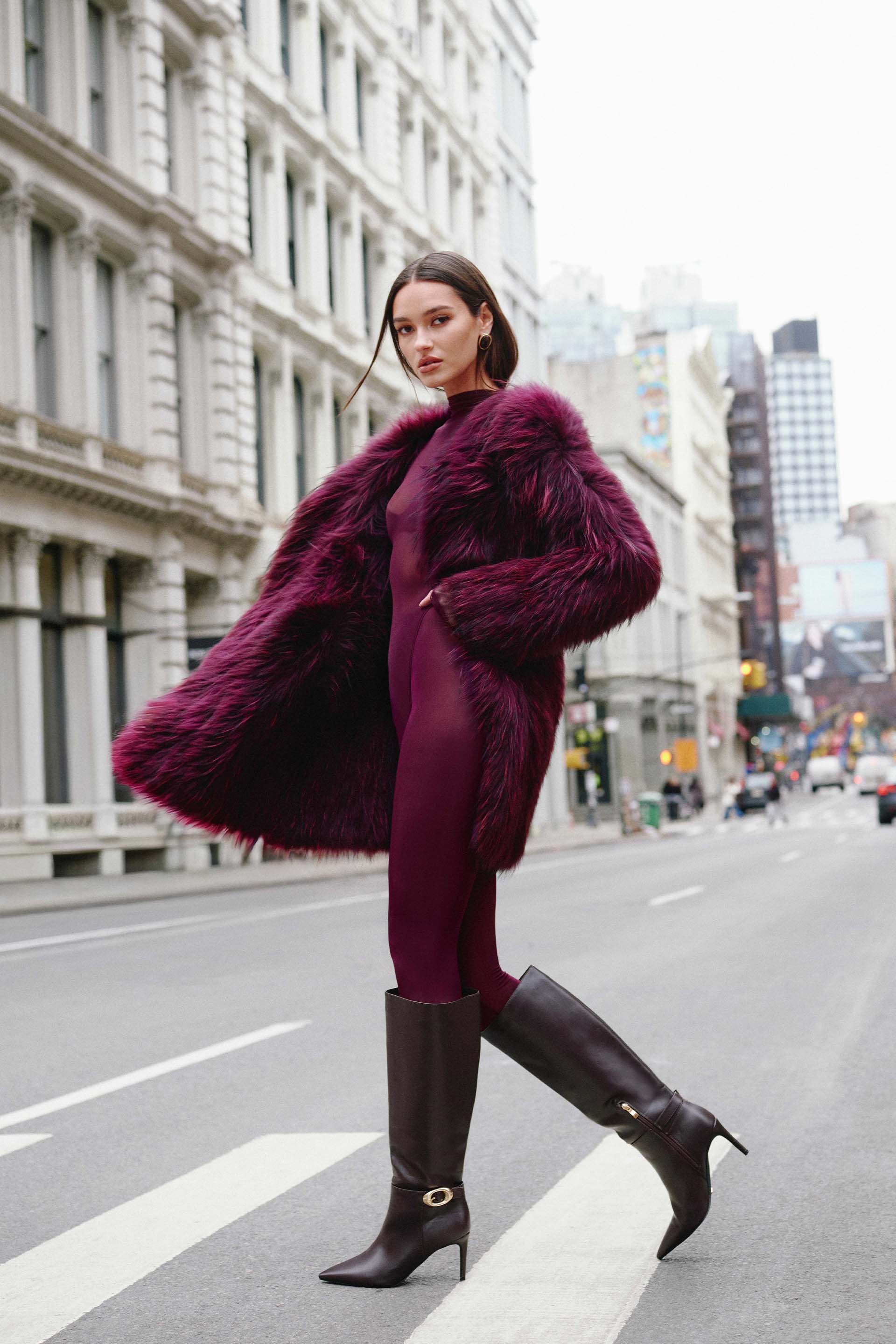 Model in a burgundy coat and boots on a city street.