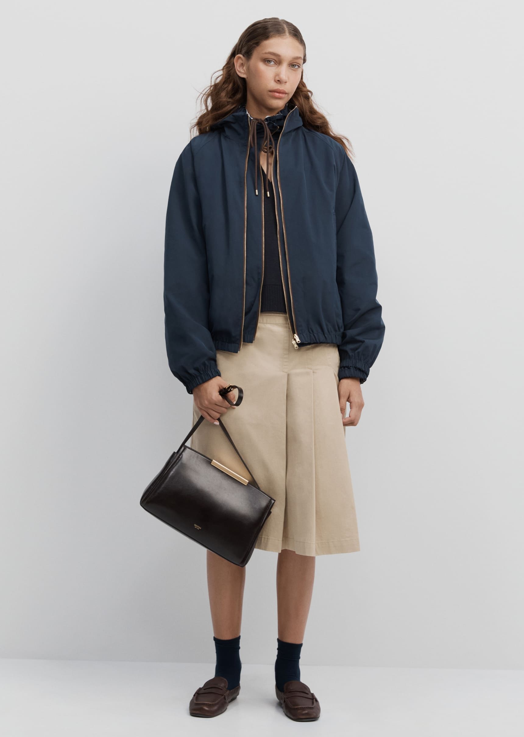 A person wearing a dark jacket, beige skirt, and holding a handbag.