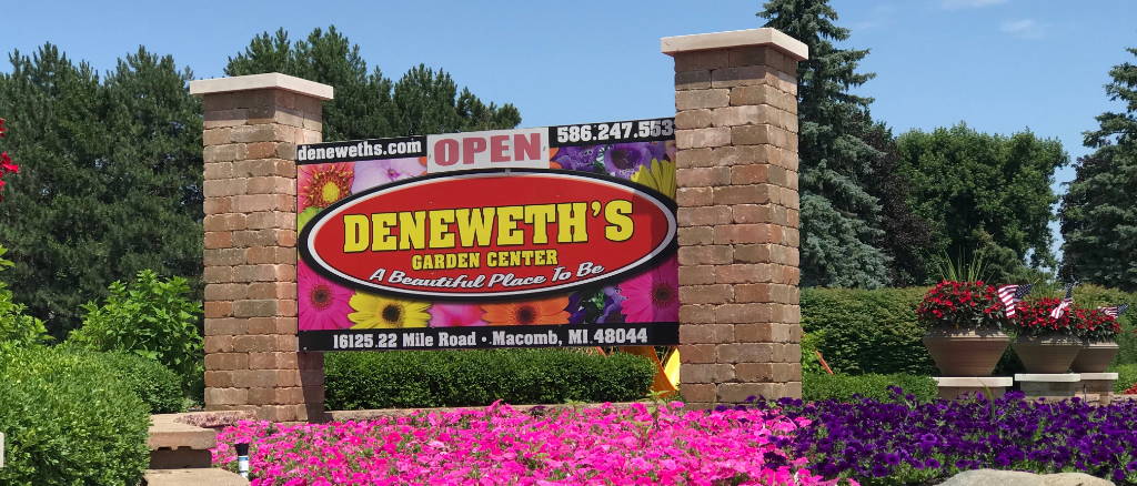 Business sign at Deneweth's Macomb in a bed of pink and purple petunias