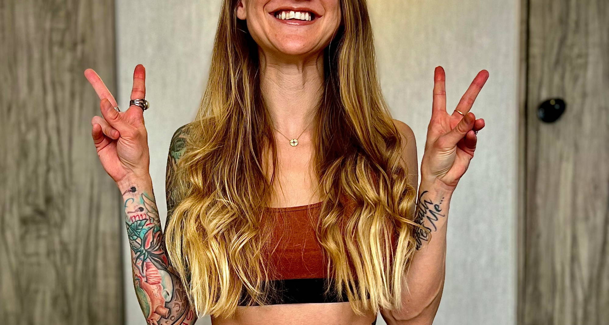 smiling woman holding up two peace signs wearing a rust-colored racerback bralette