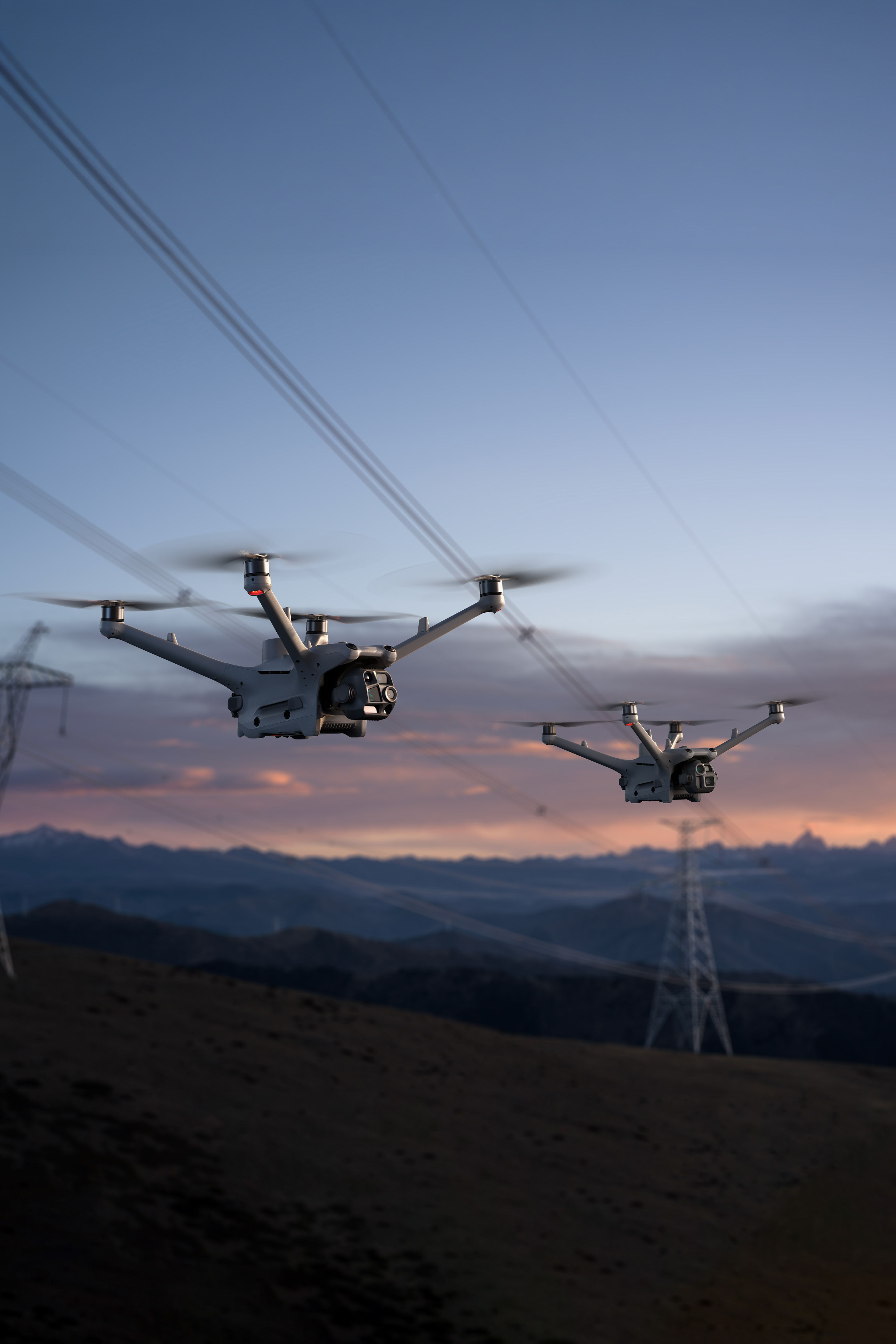 Two DJI Matrice 4D series drones flying near power lines at sunset.