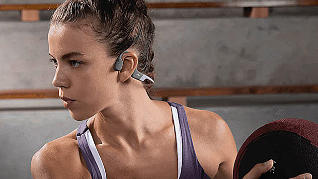 A focused athlete lifting a weight with earbuds in a gym setting.