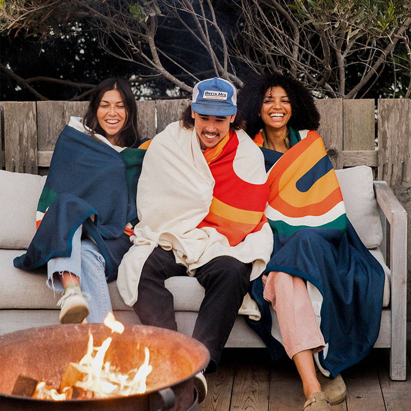 Three people wrapped in CozyHemp Blankets on couch outside