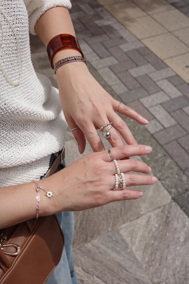 Person's hands displaying various rings and bracelets on a textured surface.