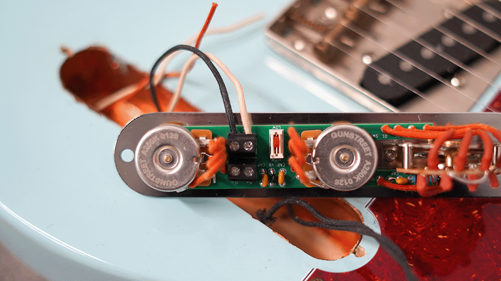 Close-up of guitar electronics with wires and circuit board on a guitar body.