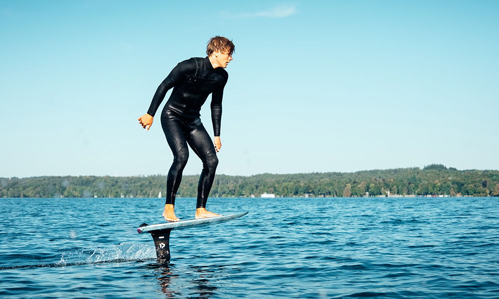 Une personne pumping sur une planche de dockstart sur l'eau, avec en arrière-plan un ciel bleu limpide.