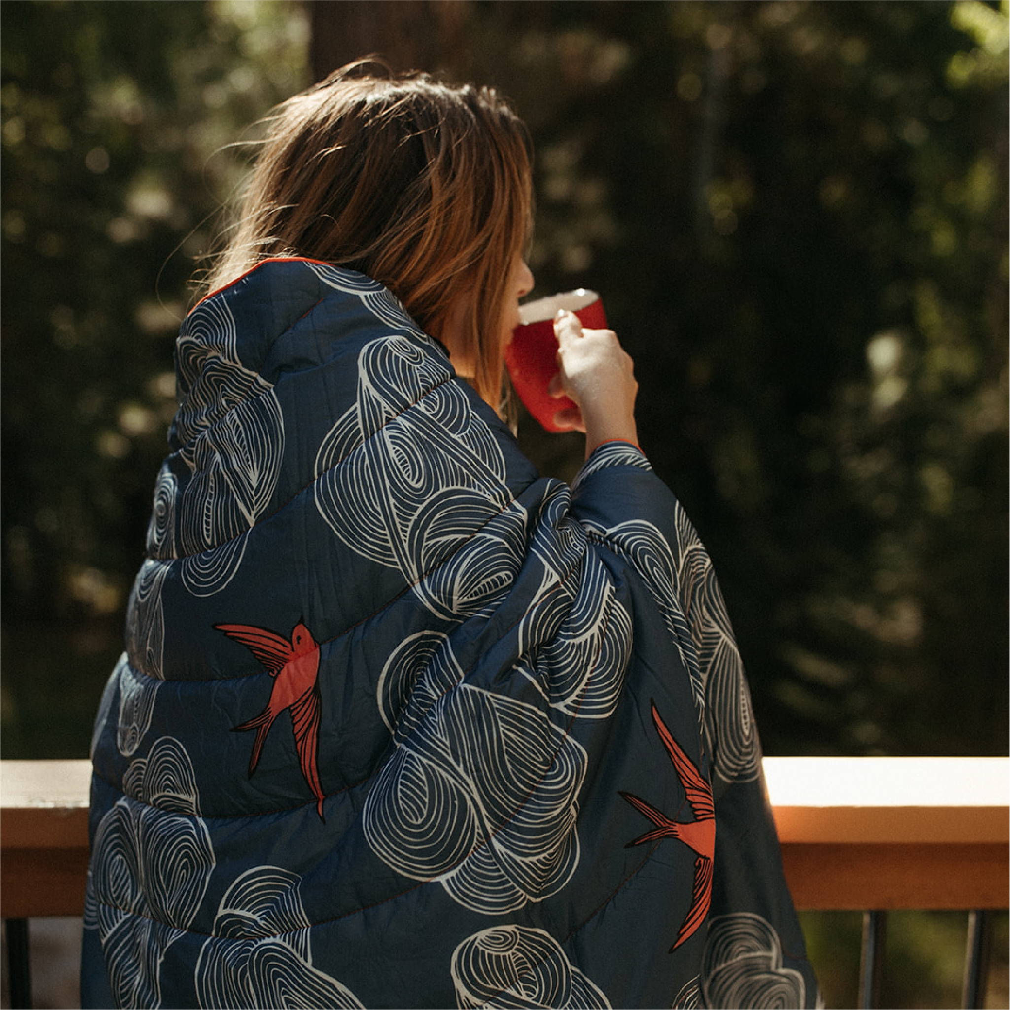 Woman wrapped in blanket drinking tea on porch