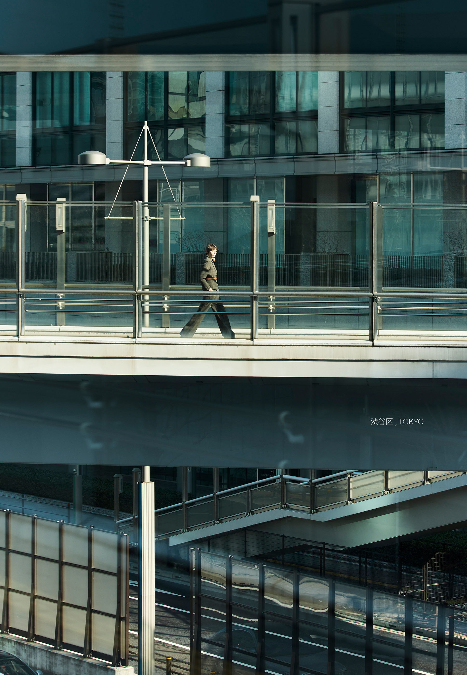 Person walking on a glass bridge with modern buildings in the background.