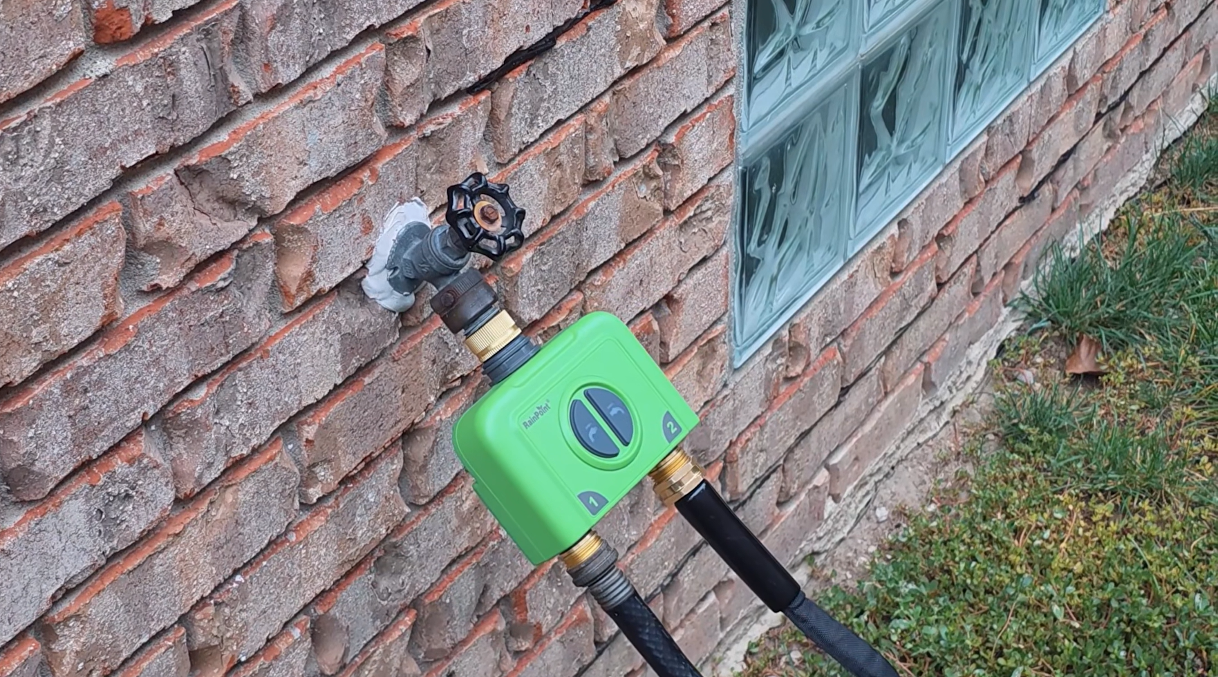 Green hose connector attached to a brick wall with a faucet handle.