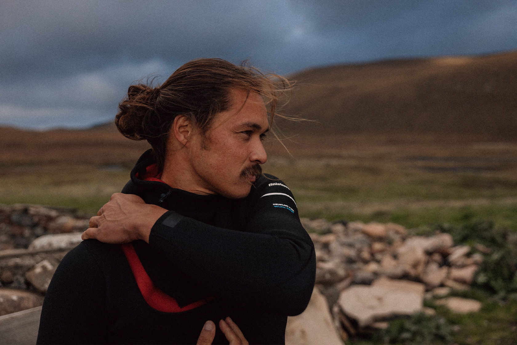 A person with a bun gazes thoughtfully in a natural landscape.
