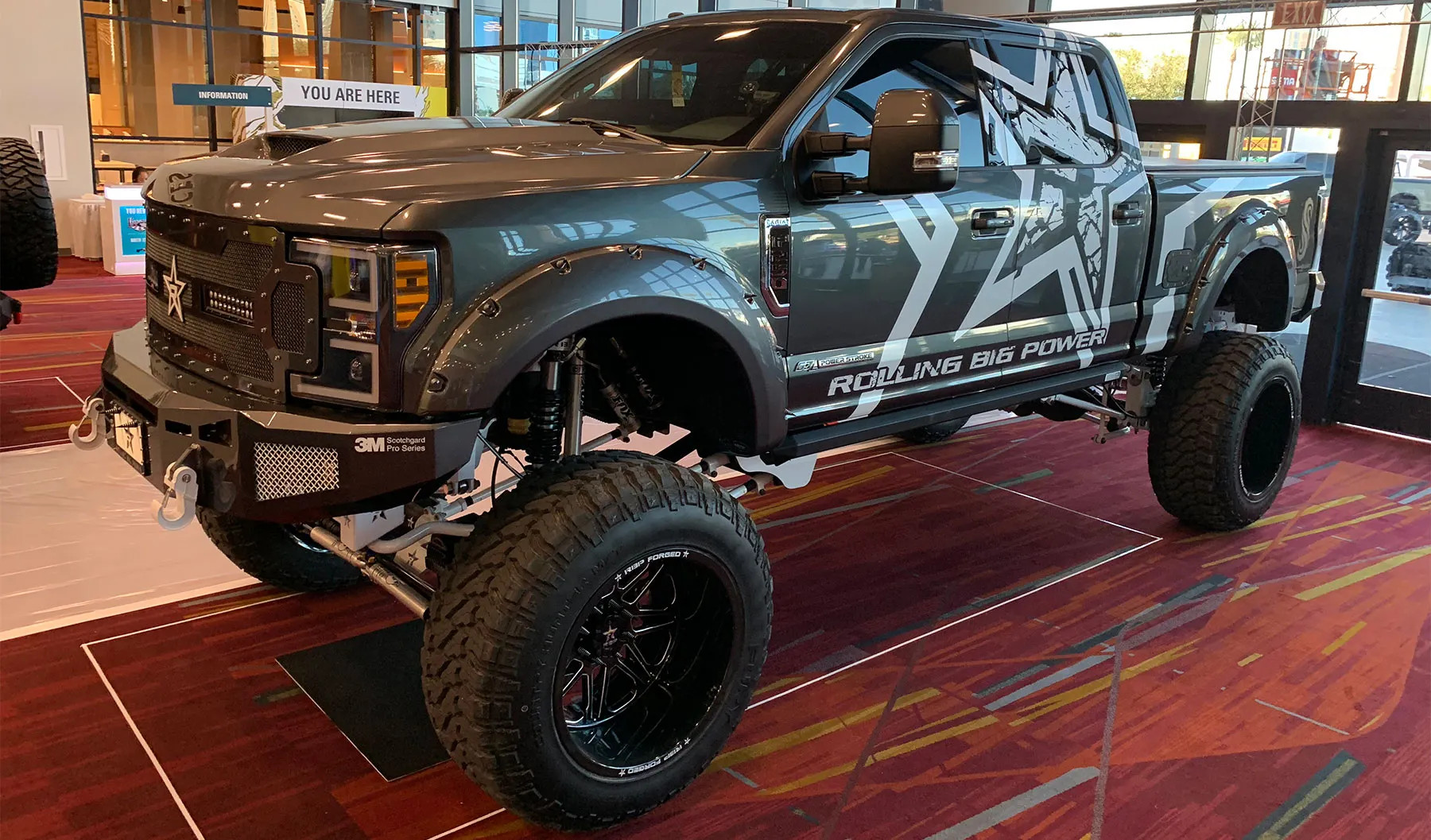 Eric's lifted gray 2018 Ford F250 Super Duty with Rolling Big Power graphics on display at an indoor automotive show