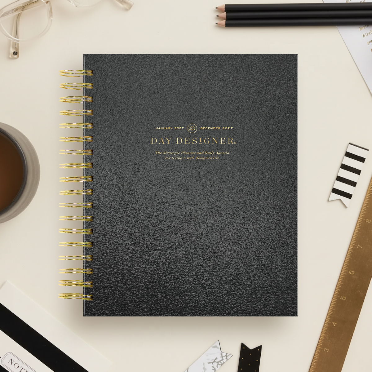 2027 day designer planner featuring black cover, gold binding on a beige background