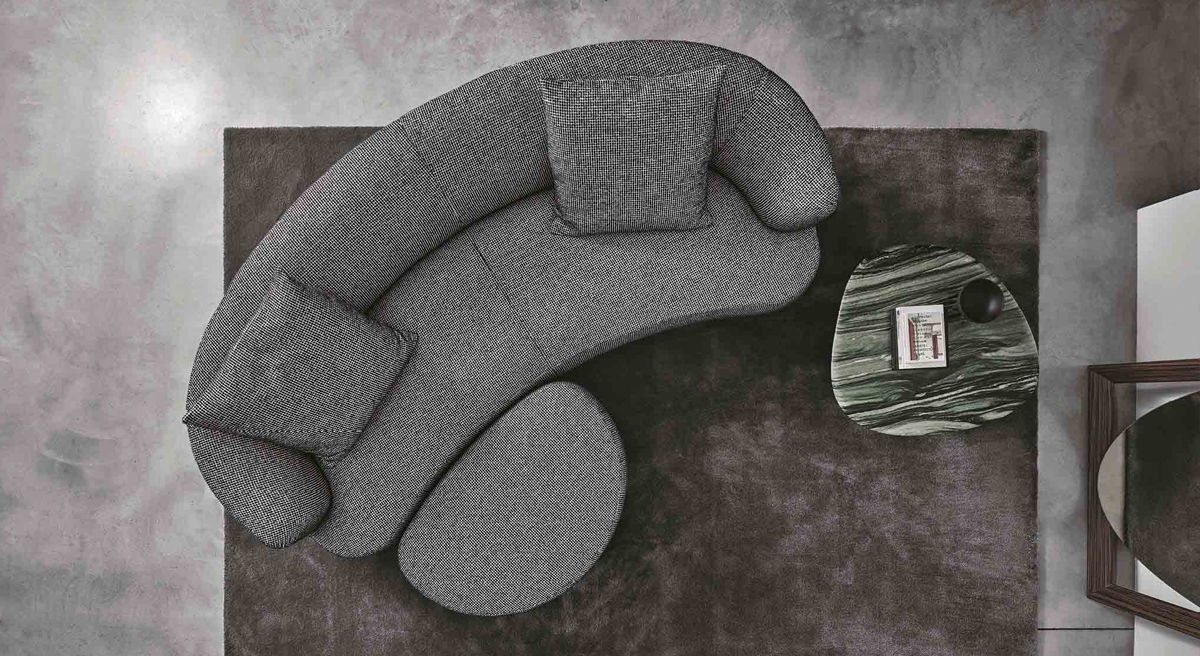 A modern grey Yves sofa by Porada on a plush rug with a side table.