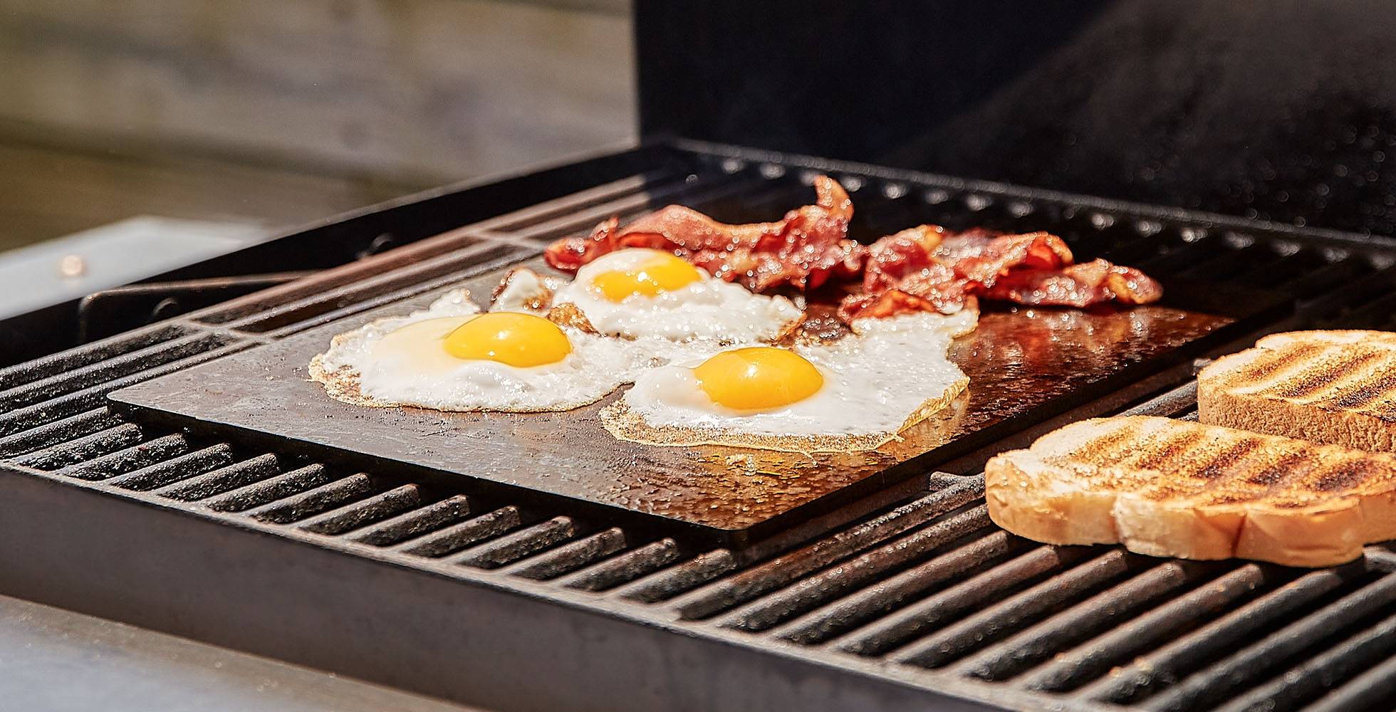A Misen Oven Steel fries eggs and bacon on an outdoor grill.