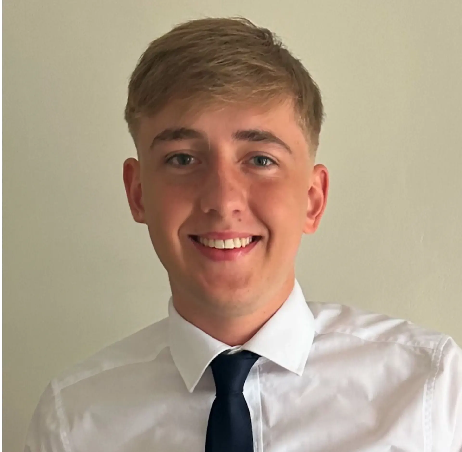 Smiling young man in a white shirt and tie against a plain background.